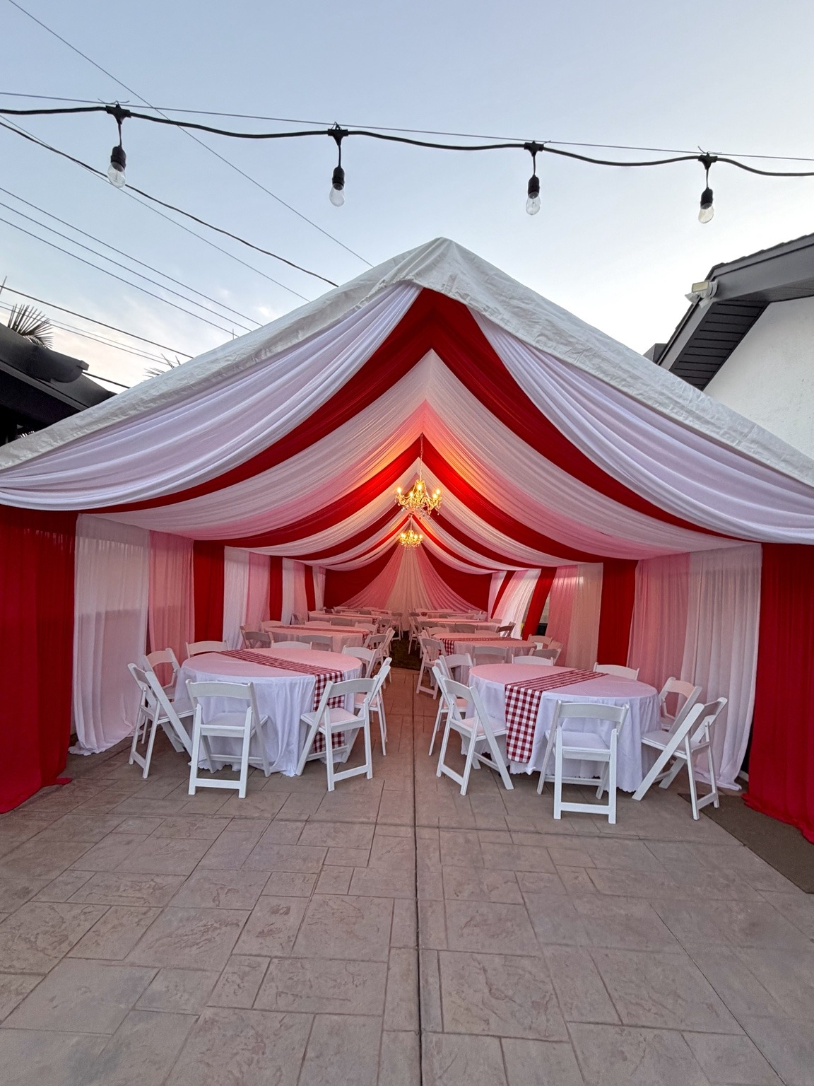 Red and white A-frame canopy draping with lit chandeliers and round tables