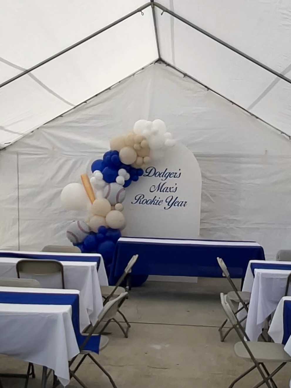 Blue and white birthday setup with tables and a balloon backdrop under a regular canopy