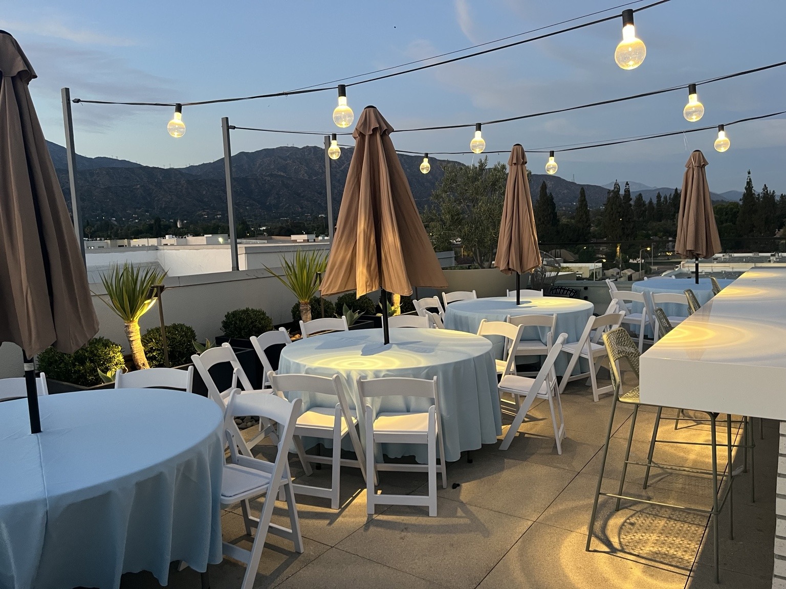 Outdoor dining tables and white chairs beneath string lights