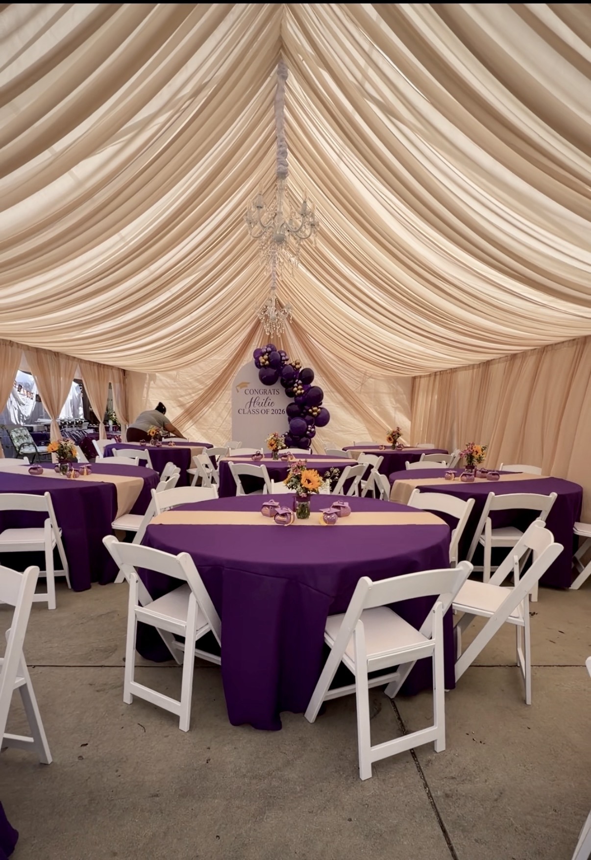 Ivory canopy draping with purple table linens and white chairs at a graduation celebration