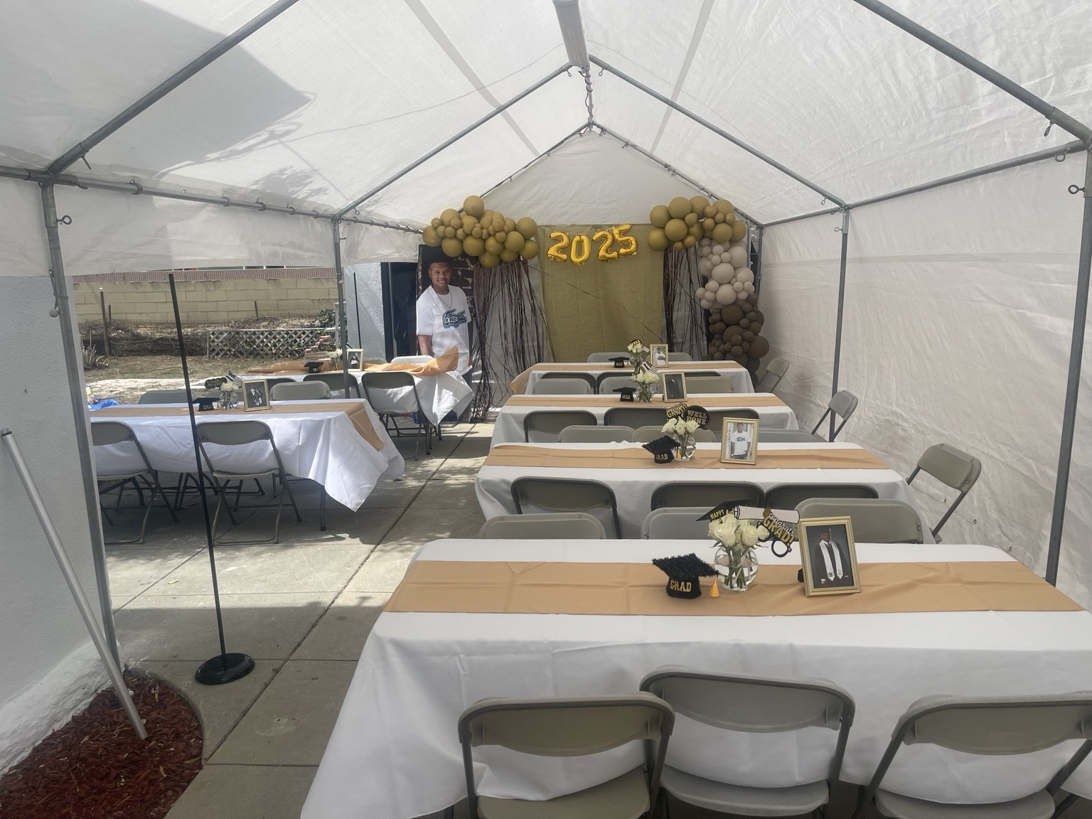 Backyard graduation celebration under a regular canopy with gold runners, tables, and chairs